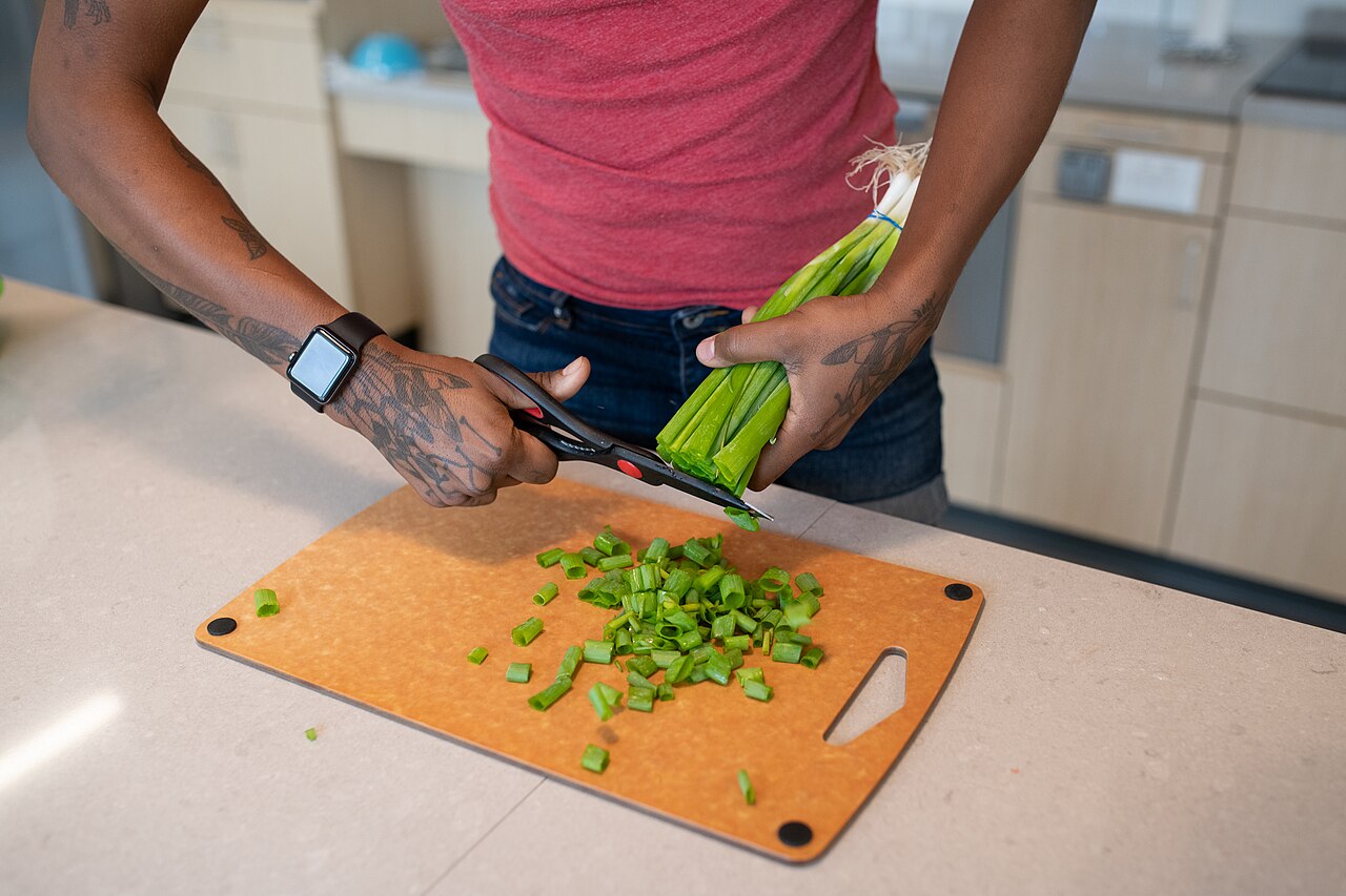 A person cutting green onions in a kitchen with adaptive scissors