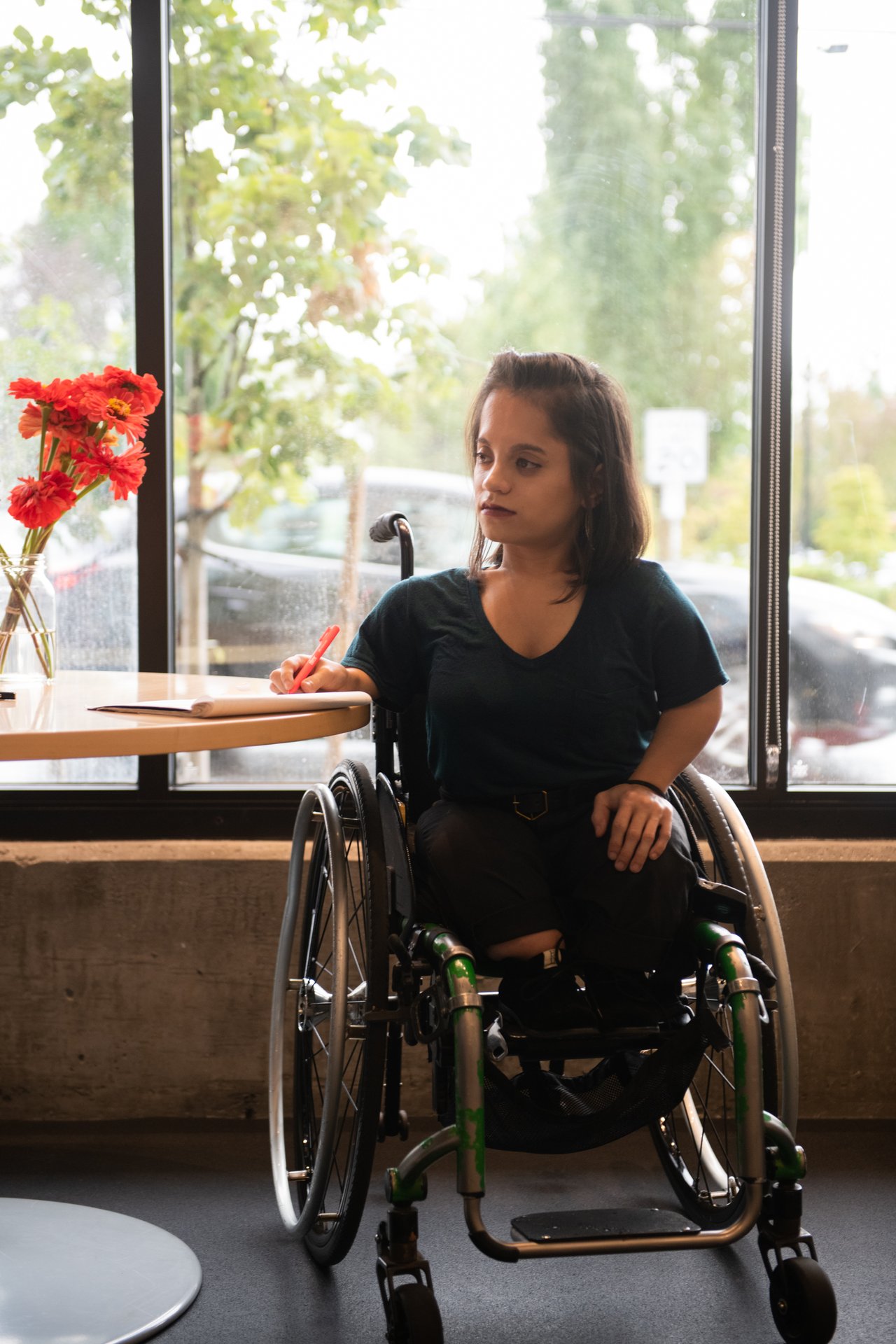 A woman in a wheelchair takes notes in front of a sunny window