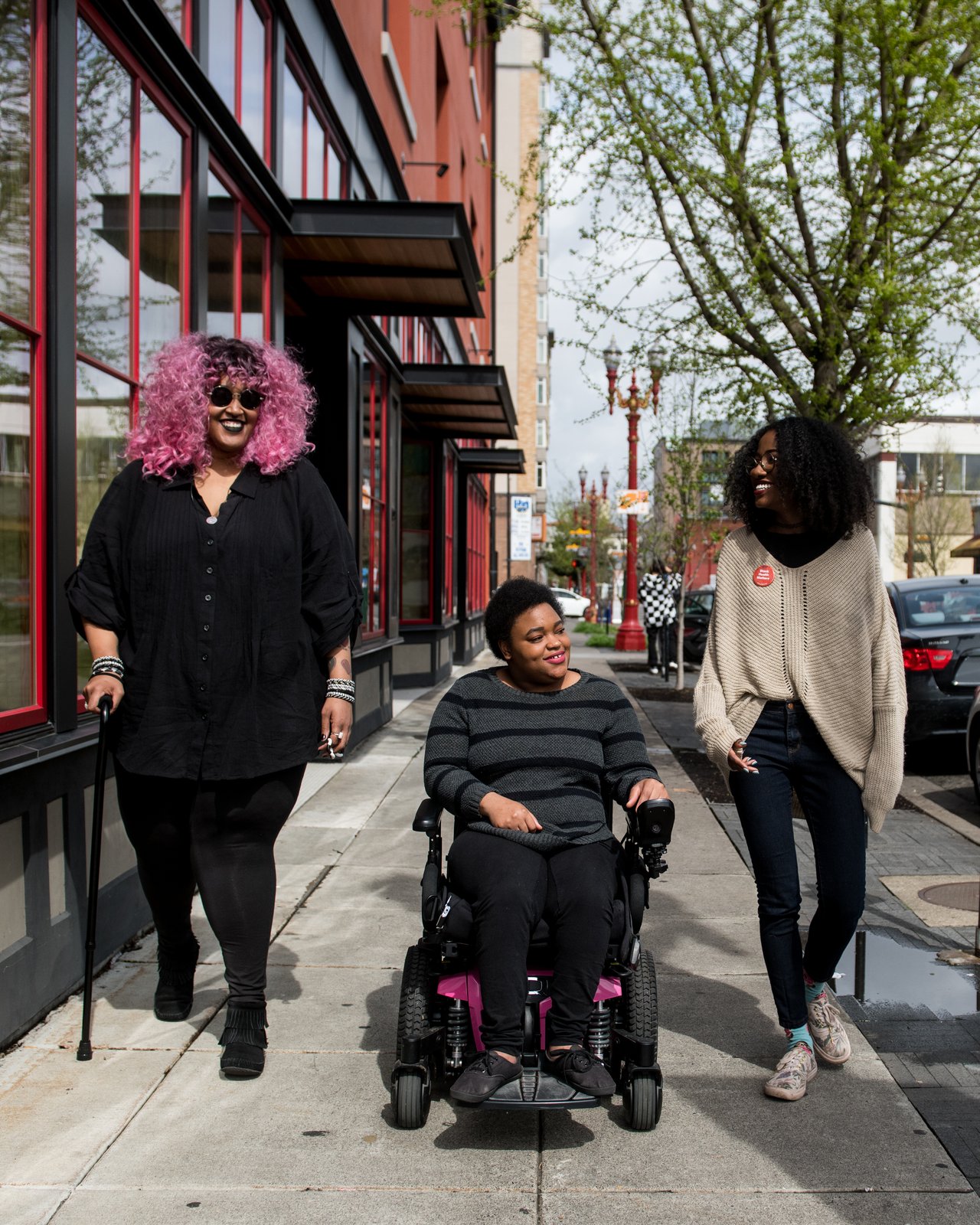 Three disabled friends smile as they walk side by side down a sidewalk