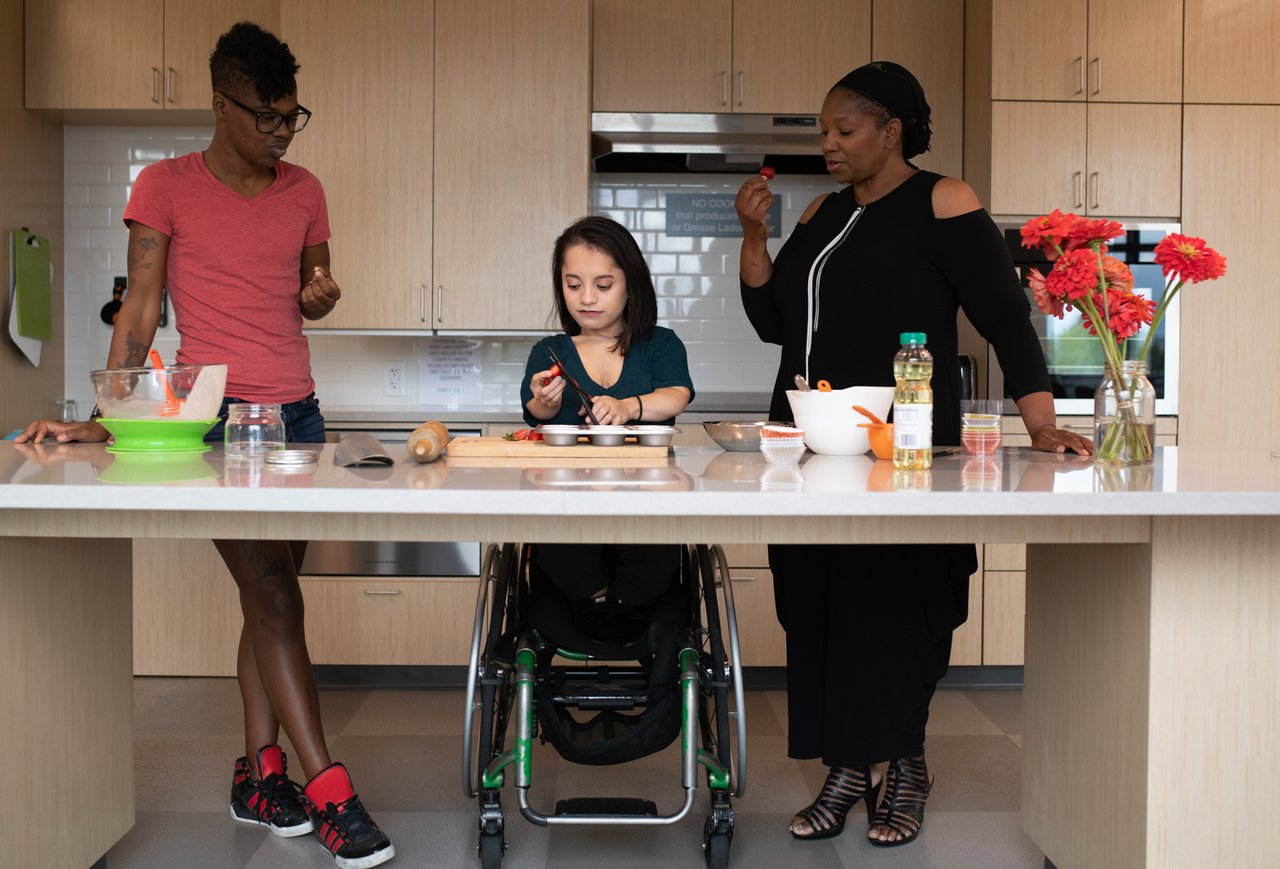 Three disabled people chop strawberries together at a kitchen counter