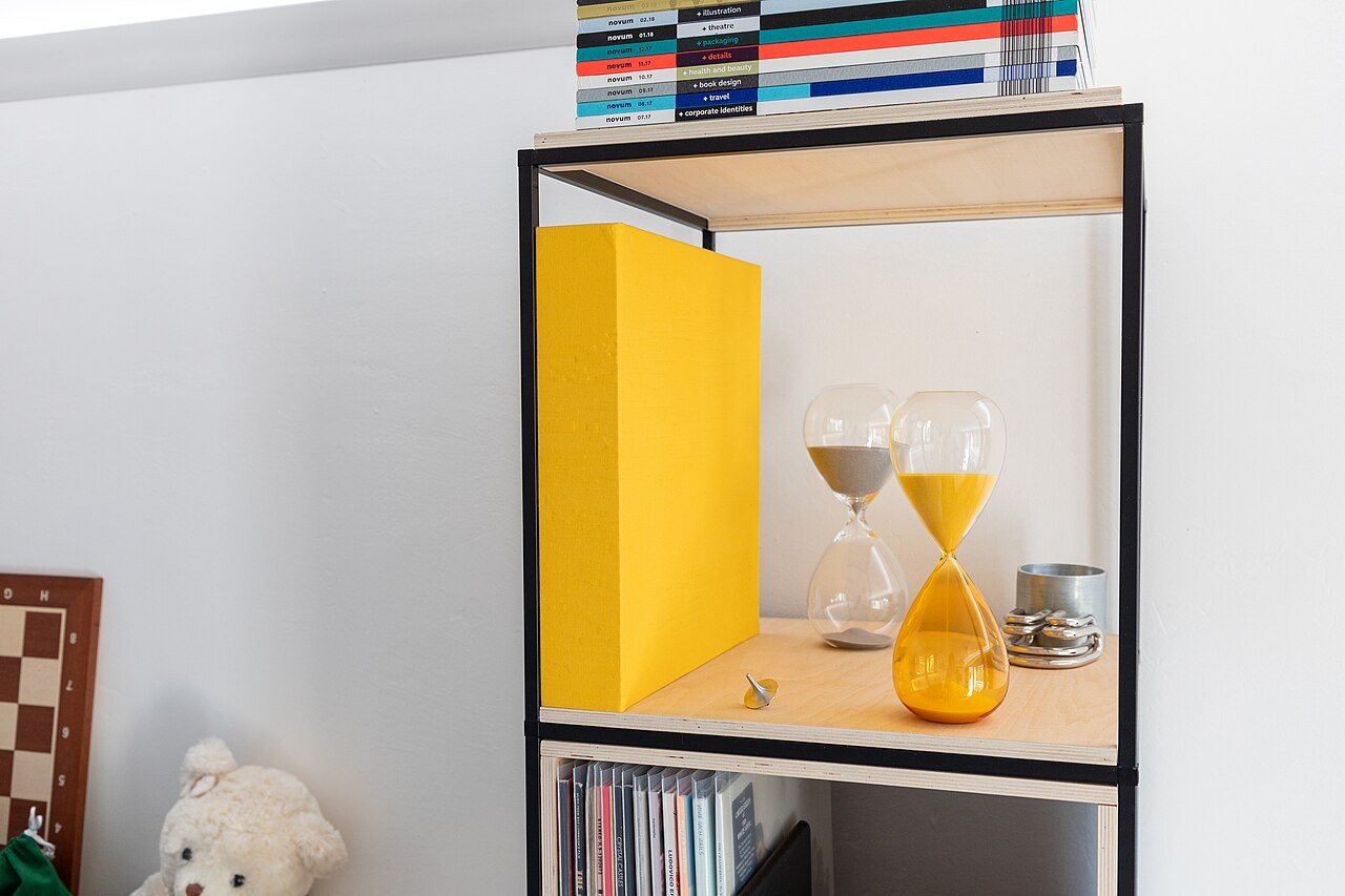Two hourglasses with flowing sand on a white bookshelf