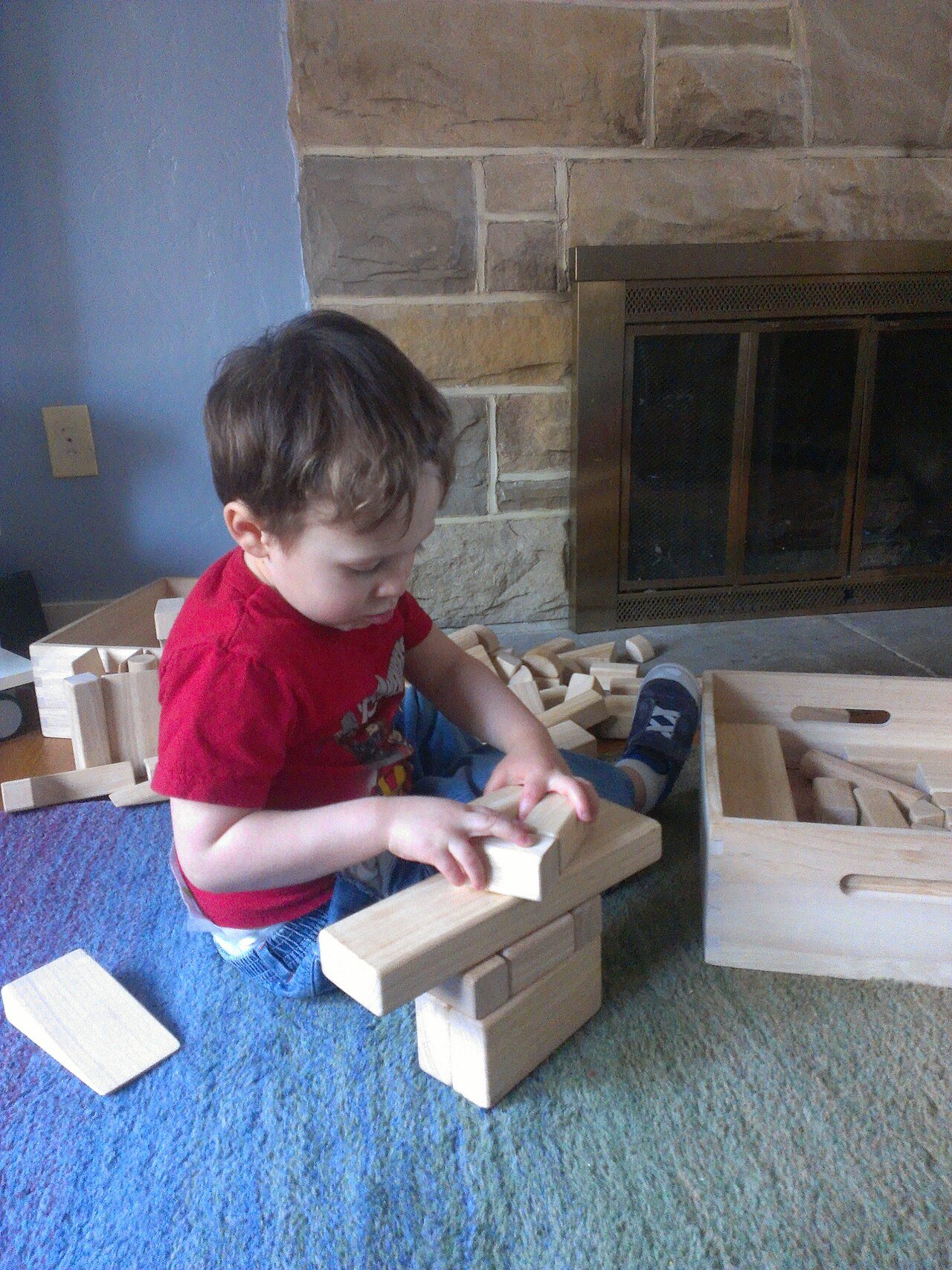 A young child stacking wooden unit blocks on a carpet at home