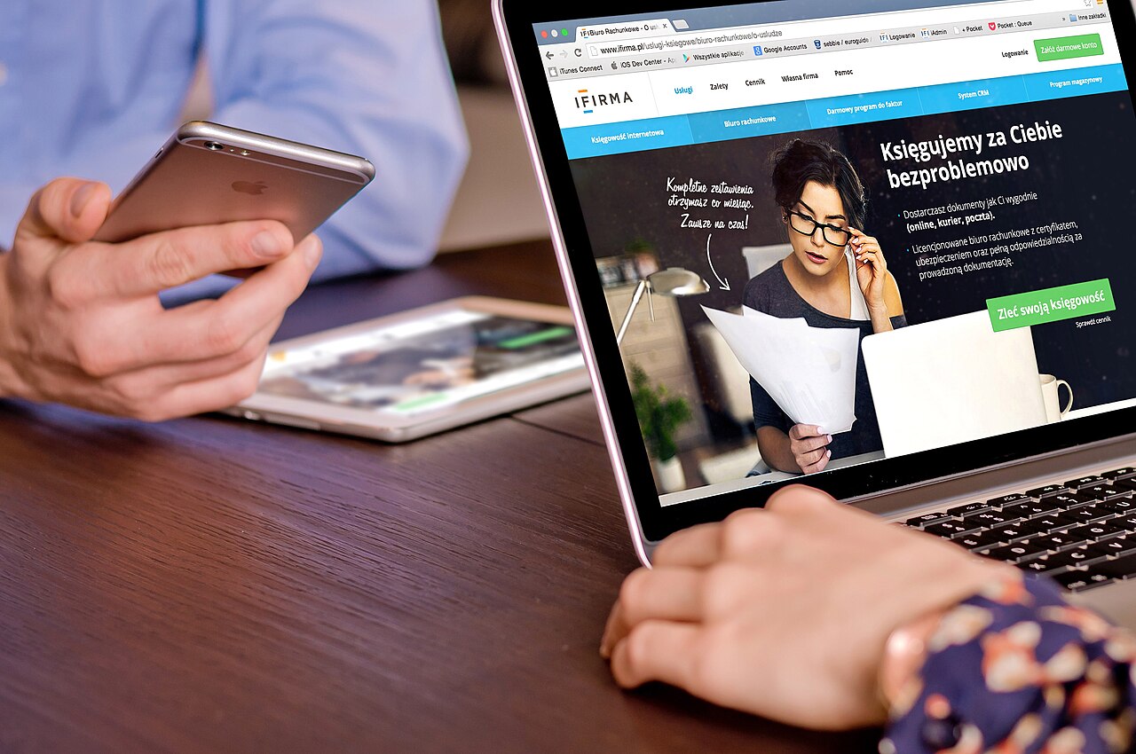 A person working on a tablet beside a laptop and smartphone