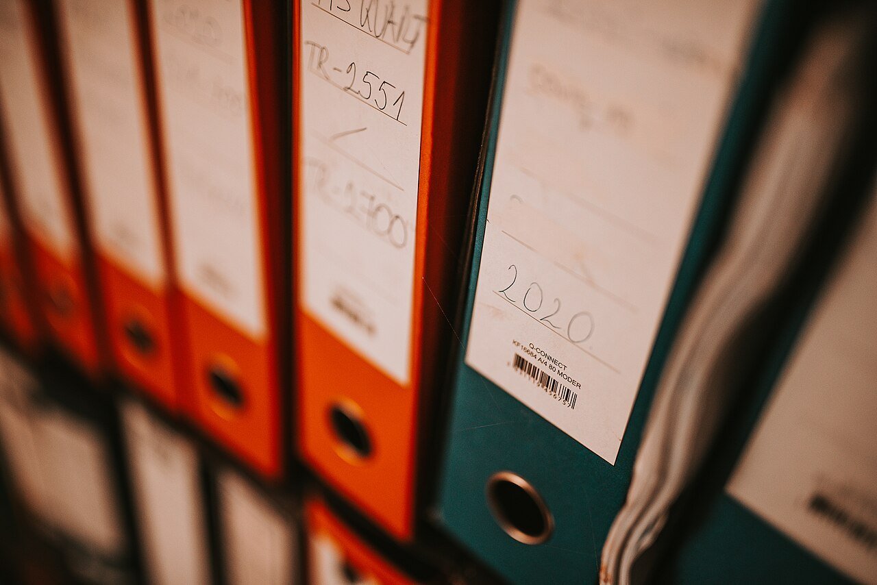 Rows of orange and green office binders with handwritten labels on a shelf