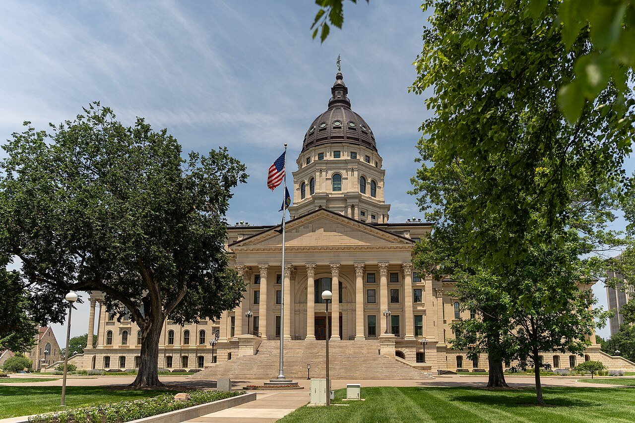 The Kansas State Capitol in Topeka on a sunny summer day, framed by trees