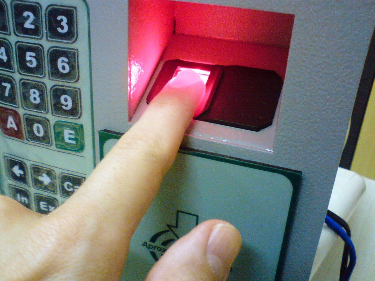 A finger pressed on a fingerprint scanner next to a keypad