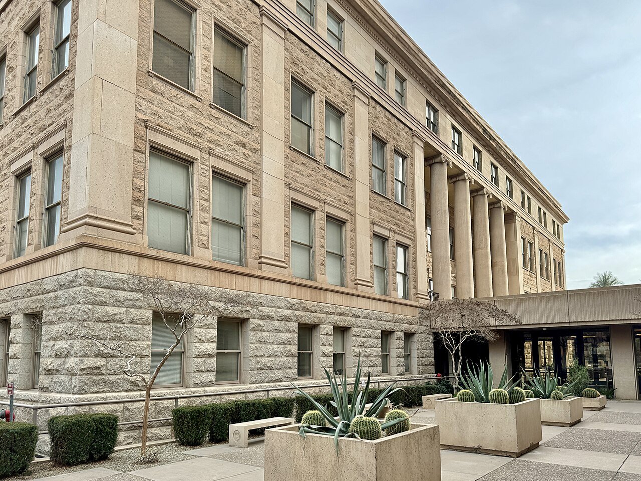 A sandstone building with tall columns at the Arizona State Capitol complex in Phoenix, with cactus planters in front