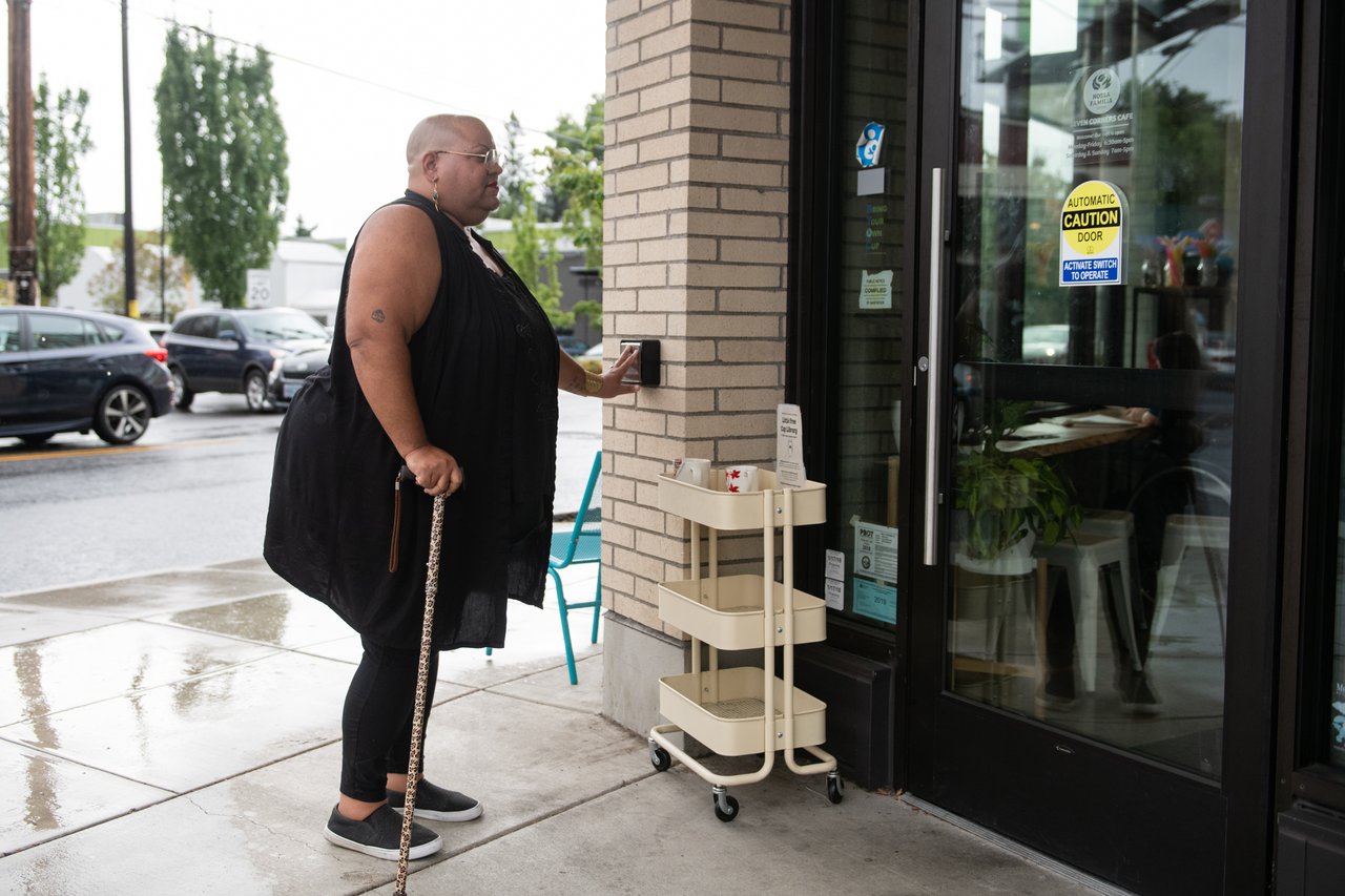 A person with a cane presses a push button to open a cafe door