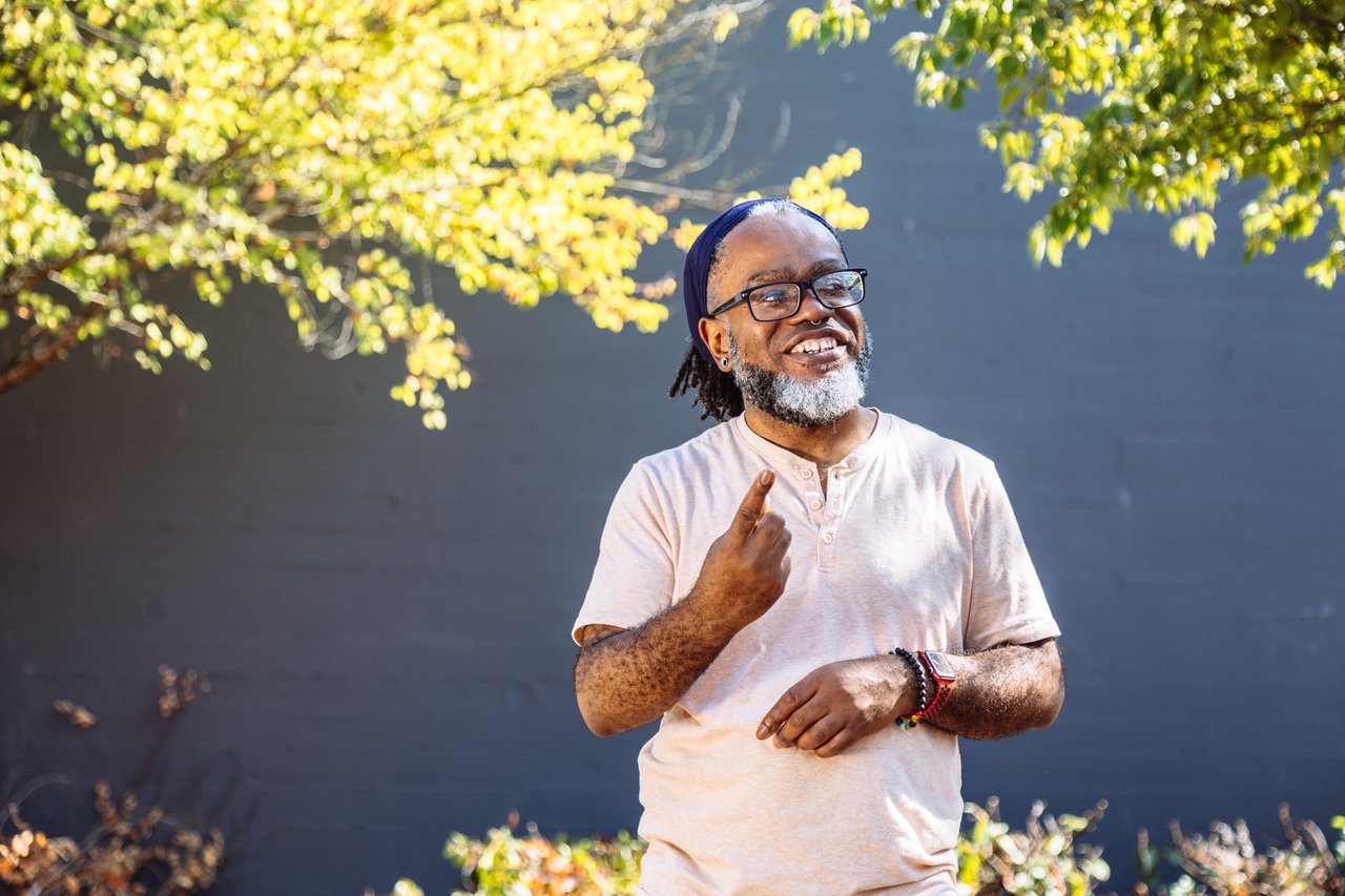 A Deaf man smiles while signing outdoors