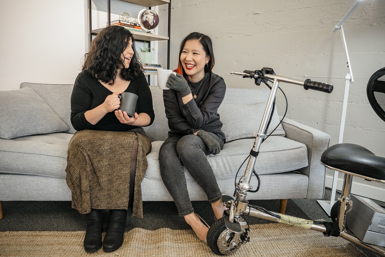 Two women laughing and holding coffee mugs on a couch