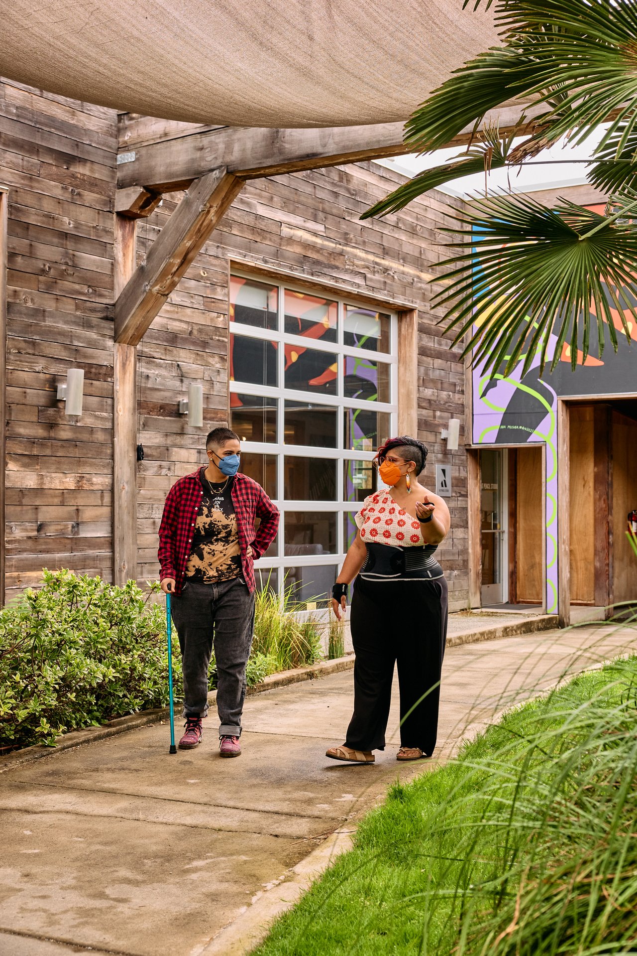 Two disabled people of color chatting as they walk through a leafy courtyard
