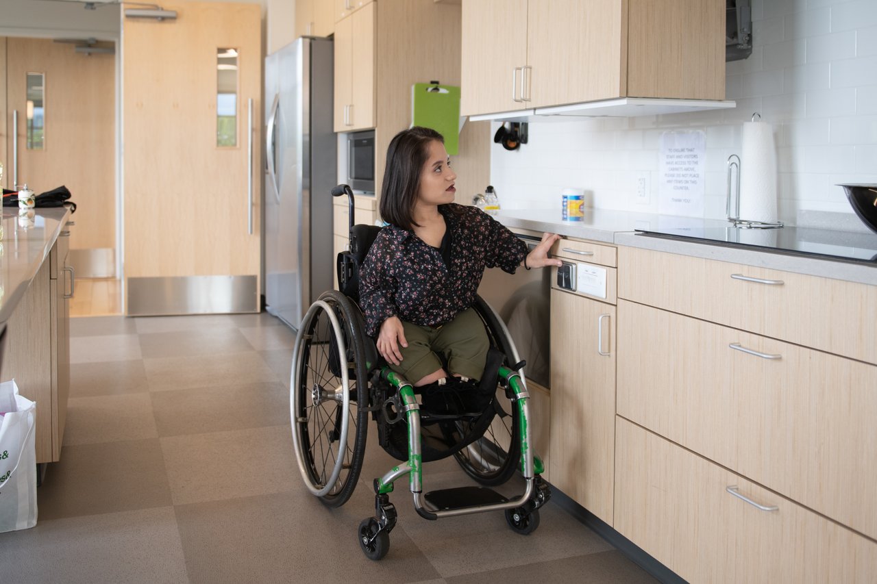 A woman using a wheelchair pulls down a height-adjustable shelf in her kitchen