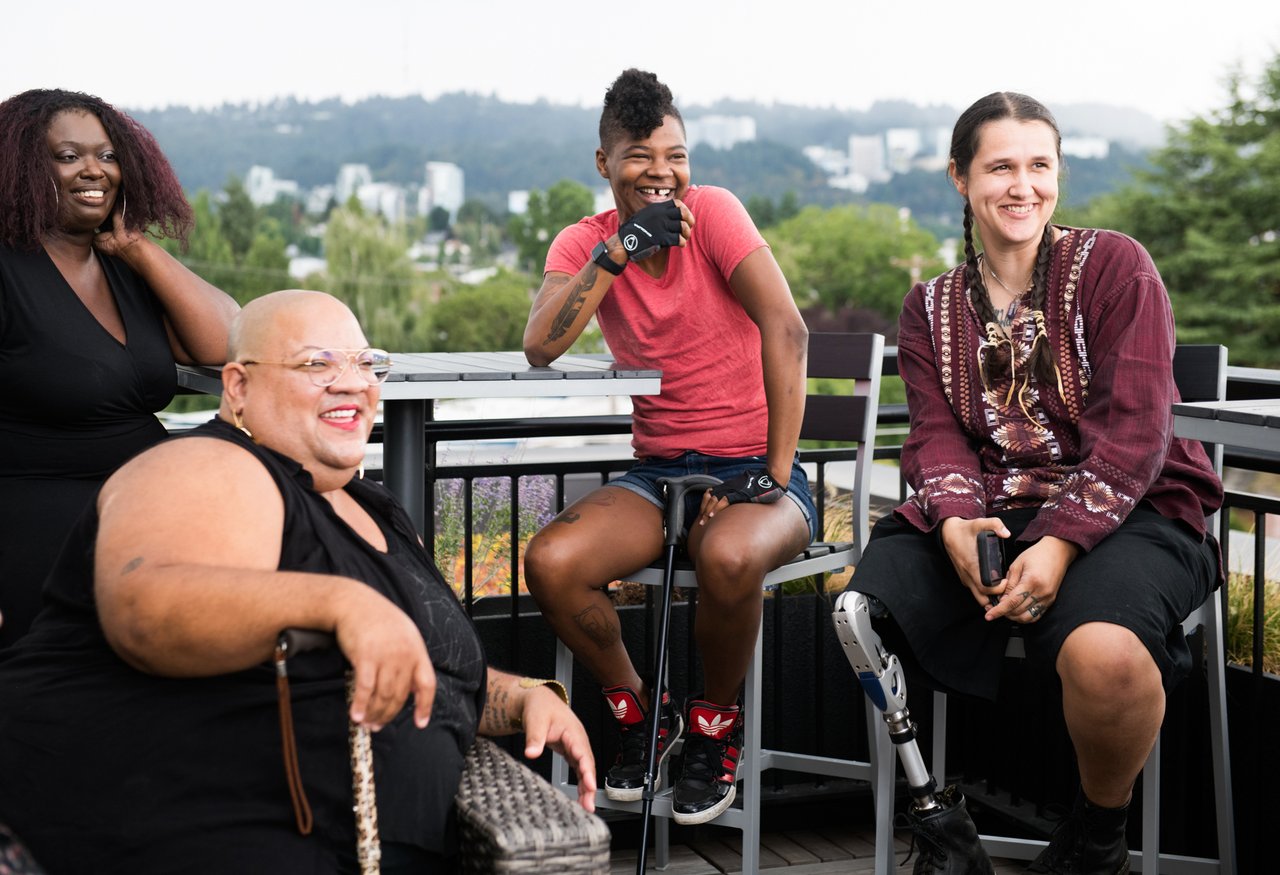 Four disabled friends with canes and prosthetic legs laugh together on a rooftop deck