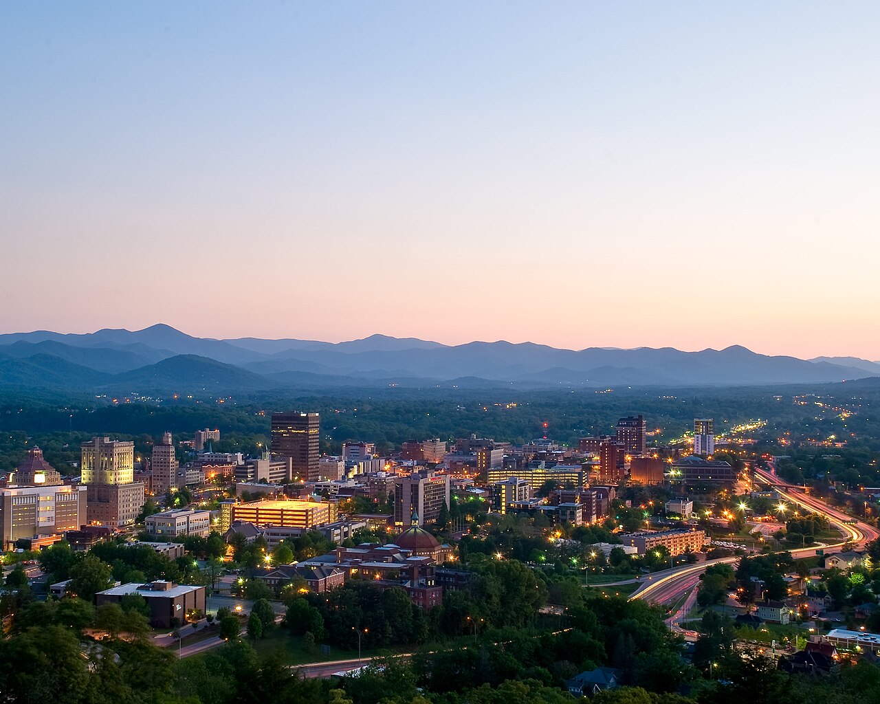 Downtown Asheville, North Carolina, at dusk with the Blue Ridge Mountains behind it