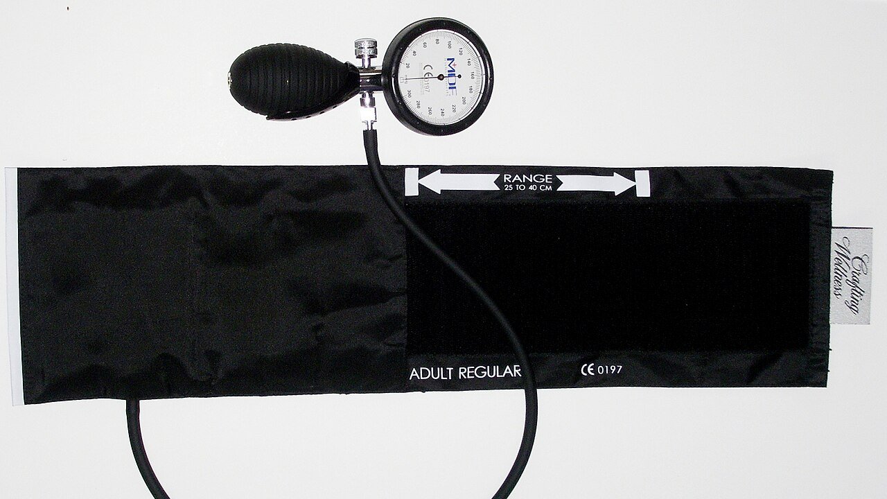 An aneroid blood pressure gauge and cuff laid out on a white surface